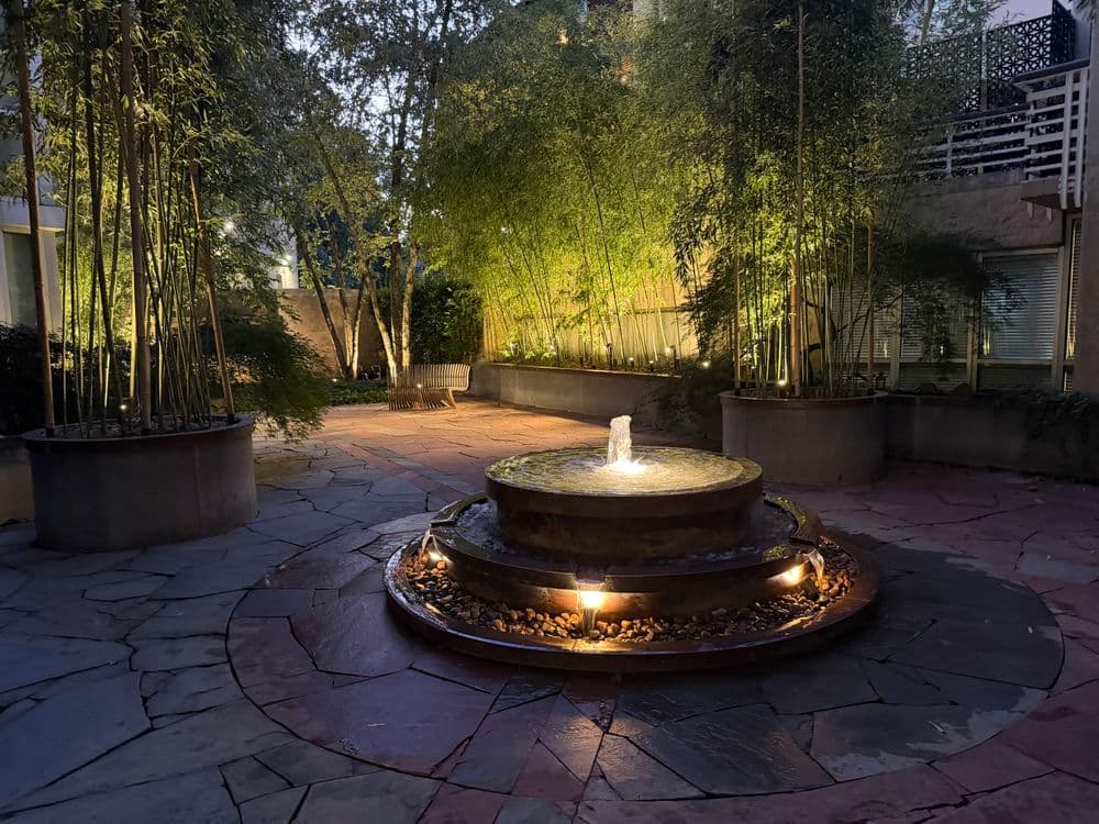 Serene outdoor garden with a stone fountain surrounded by bamboo and soft lighting.