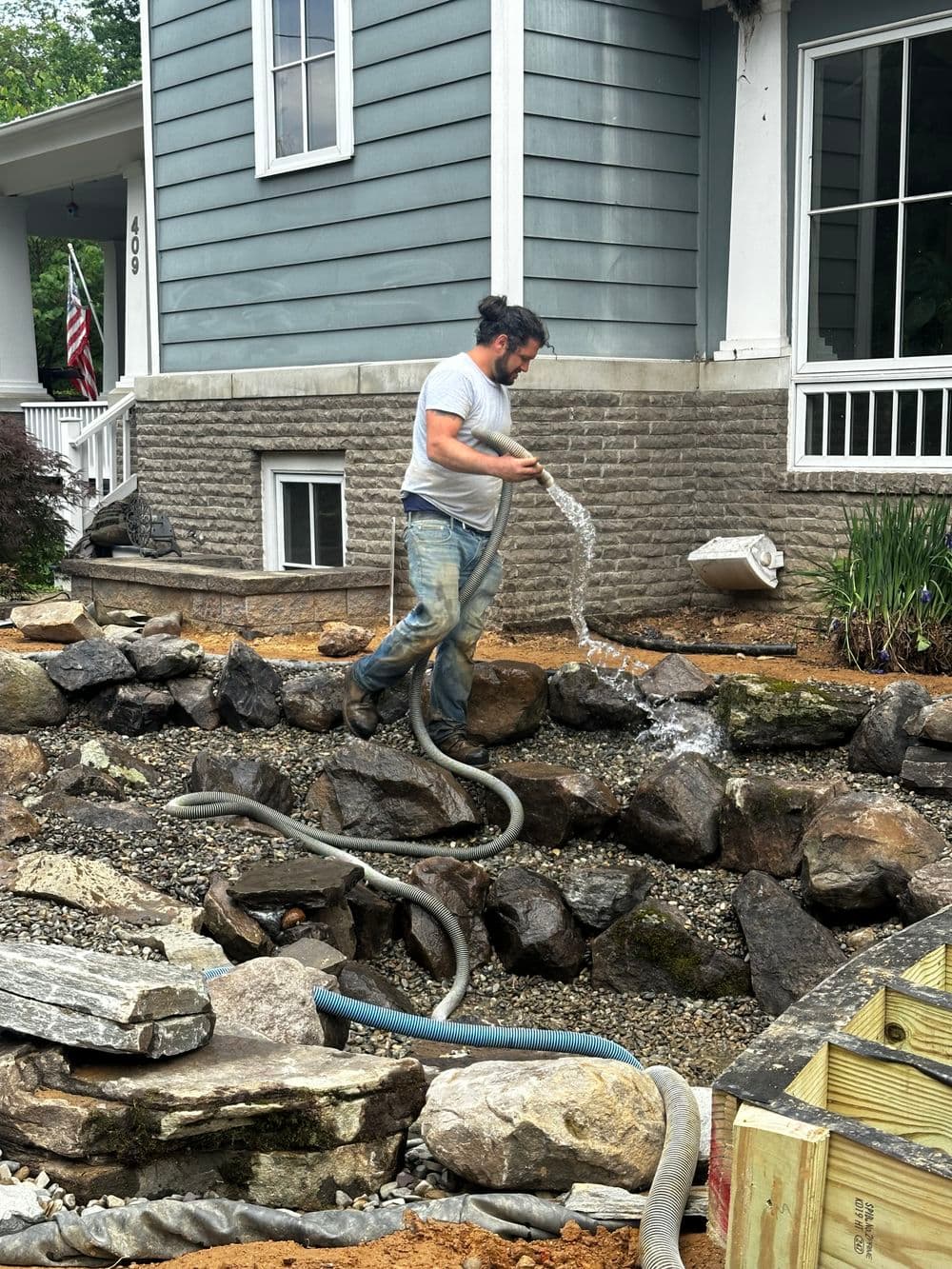 Man pumping water from a stone-filled area near a house with landscaping in progress.