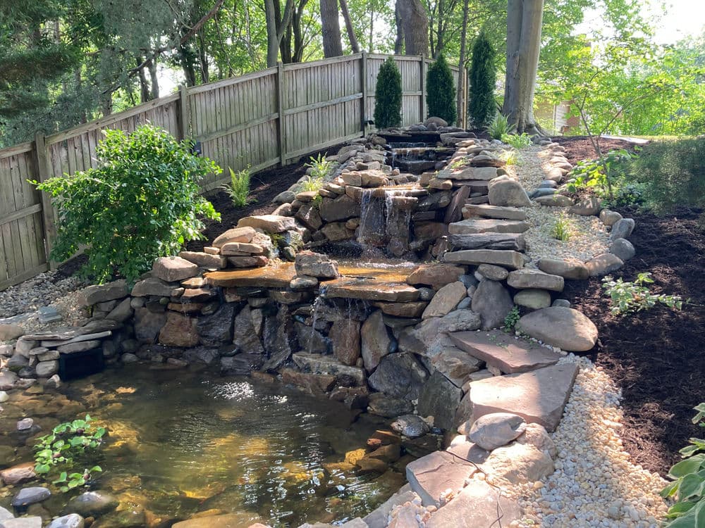 Serene backyard waterfall with stone features, lush greenery, and tranquil pond.