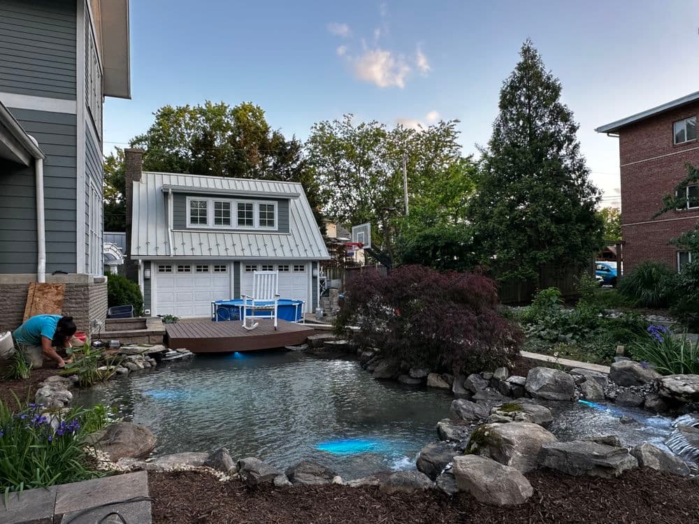Home exterior with a serene water feature, landscaped garden, and a modern garage.