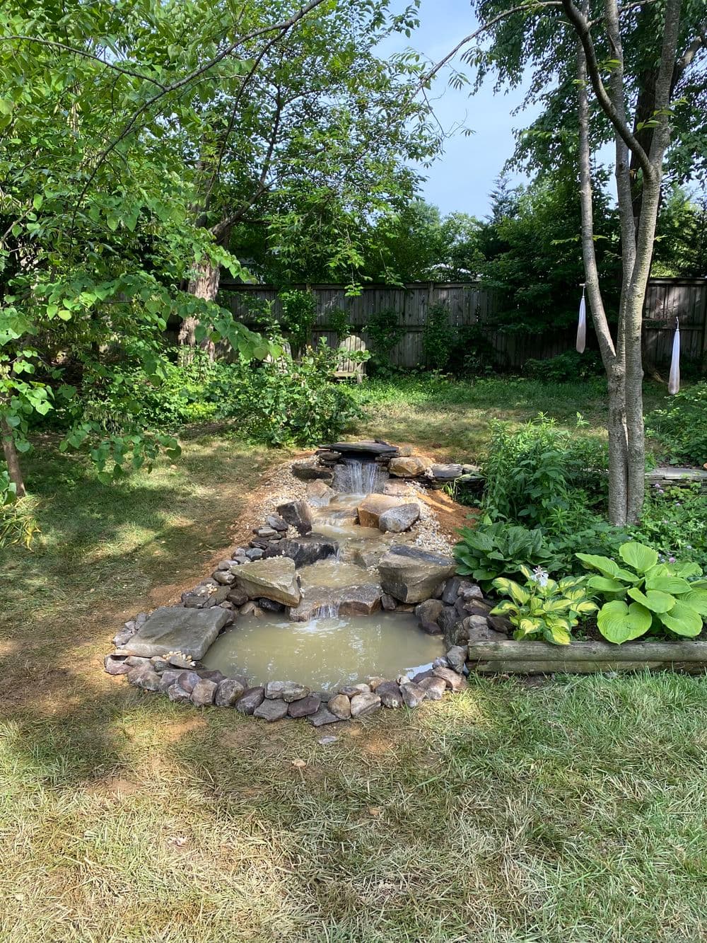 Tranquil backyard waterfall with rocks, pond, and lush greenery in a serene garden setting.